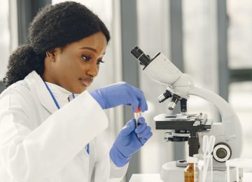 Medical doctor girl working with a microscope. Young female scientist doing vaccine research.